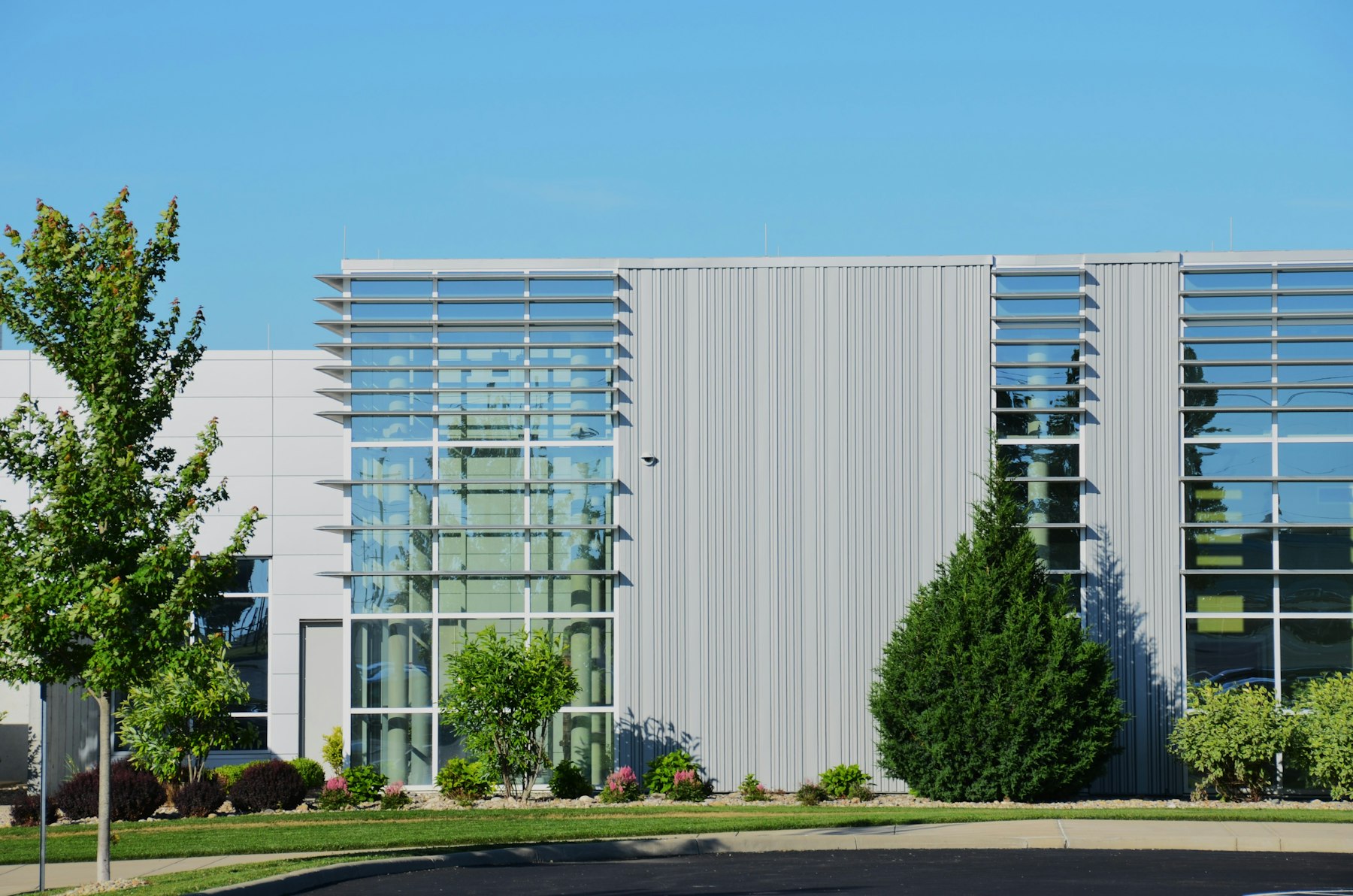 Modern commercial building entrance softened by ornamental trees, shrub beds, and a crisp strip of lawn