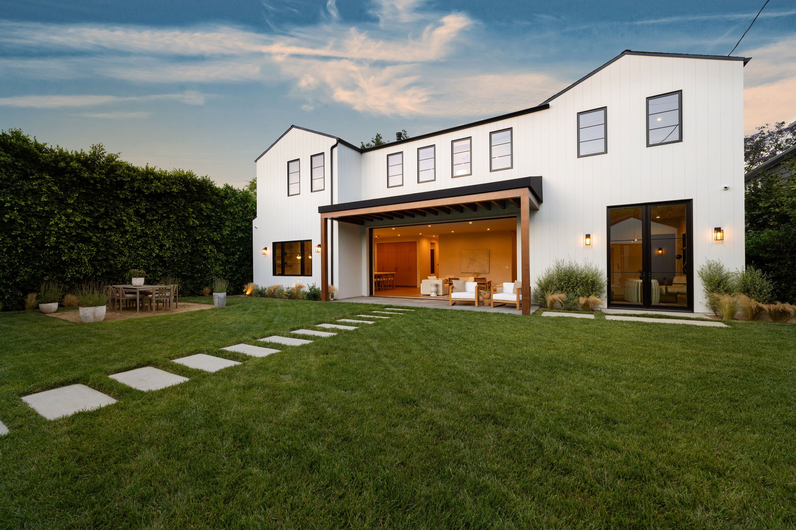 Artificial turf backyard with outdoor dining table and bar seating at dusk